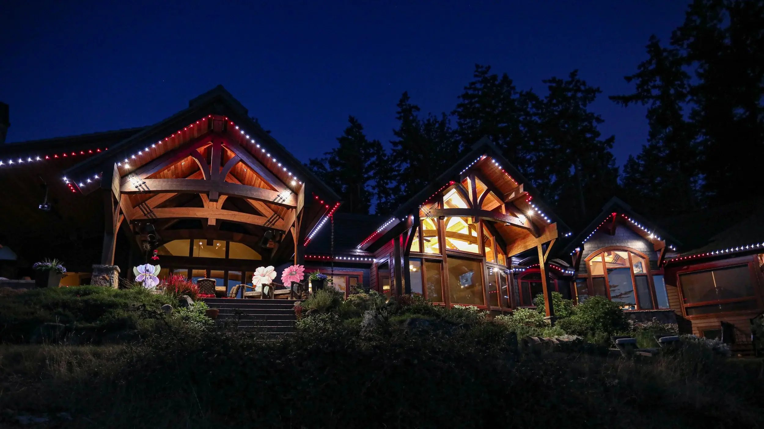 Luxury timber-frame home illuminated with red and white permanent outdoor lighting at night