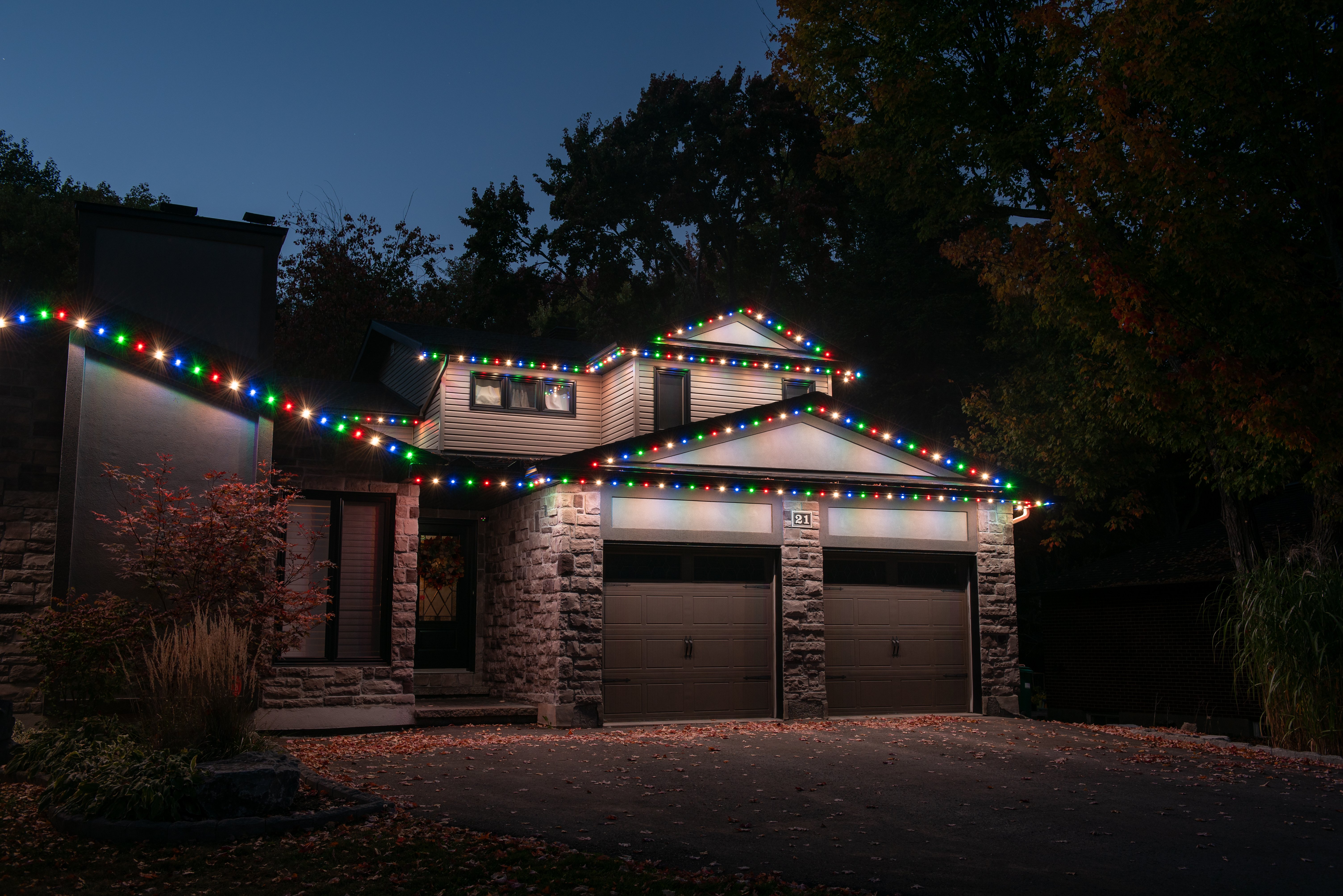 Residential home with multicolor permanent holiday lighting displayed across the roofline at night