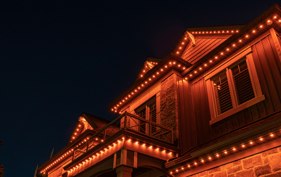 Close-up of a home’s roofline illuminated with orange Permanent Holiday Lighting for a warm, spooky Halloween look.