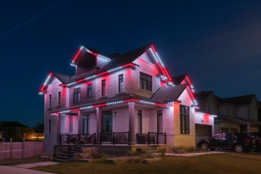 Residential home illuminated with permanent Christmas lighting in red and white