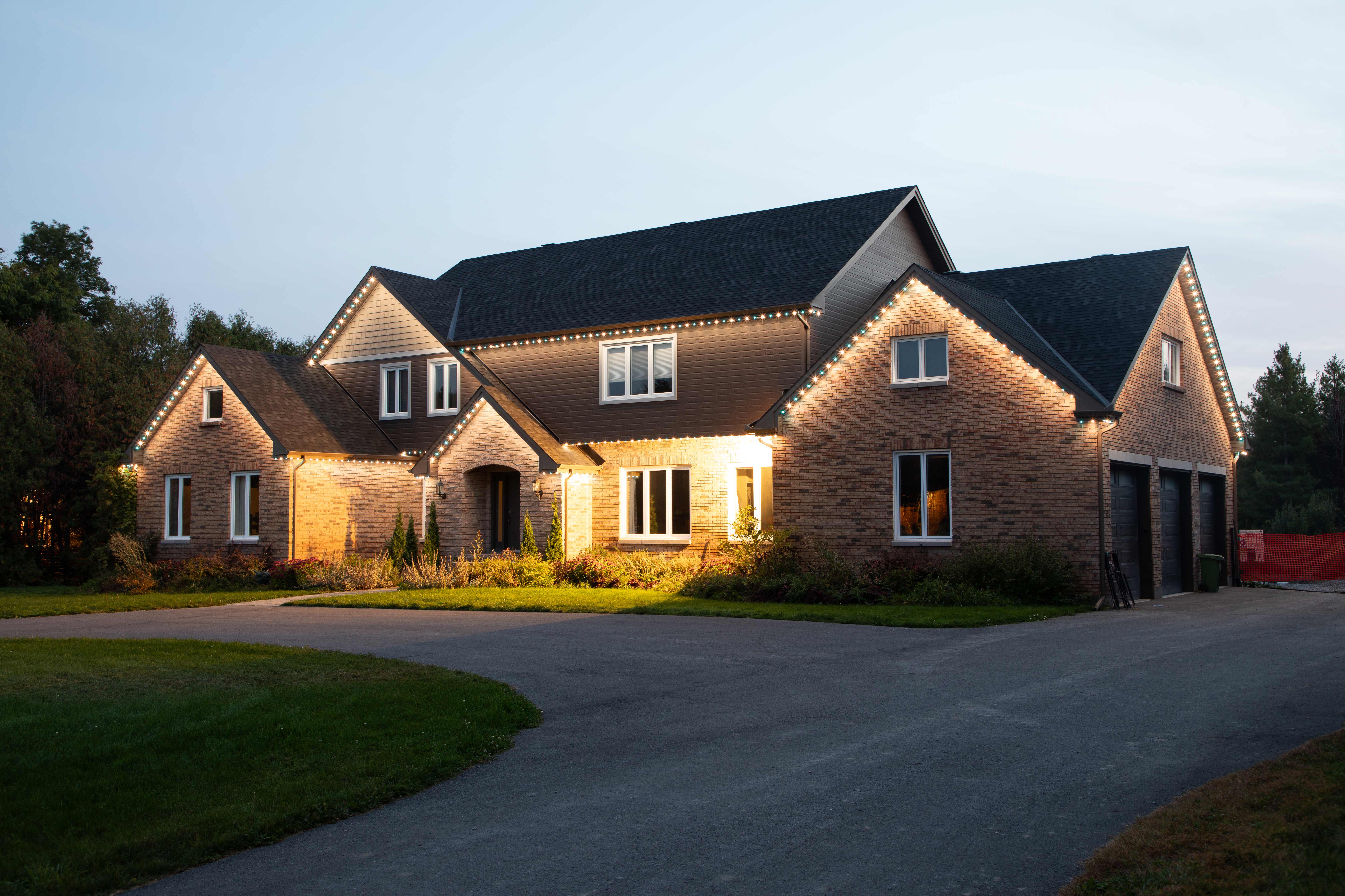 Red, green, and white permanent Christmas lights outlining the roofline of a house in a festive winter scene.