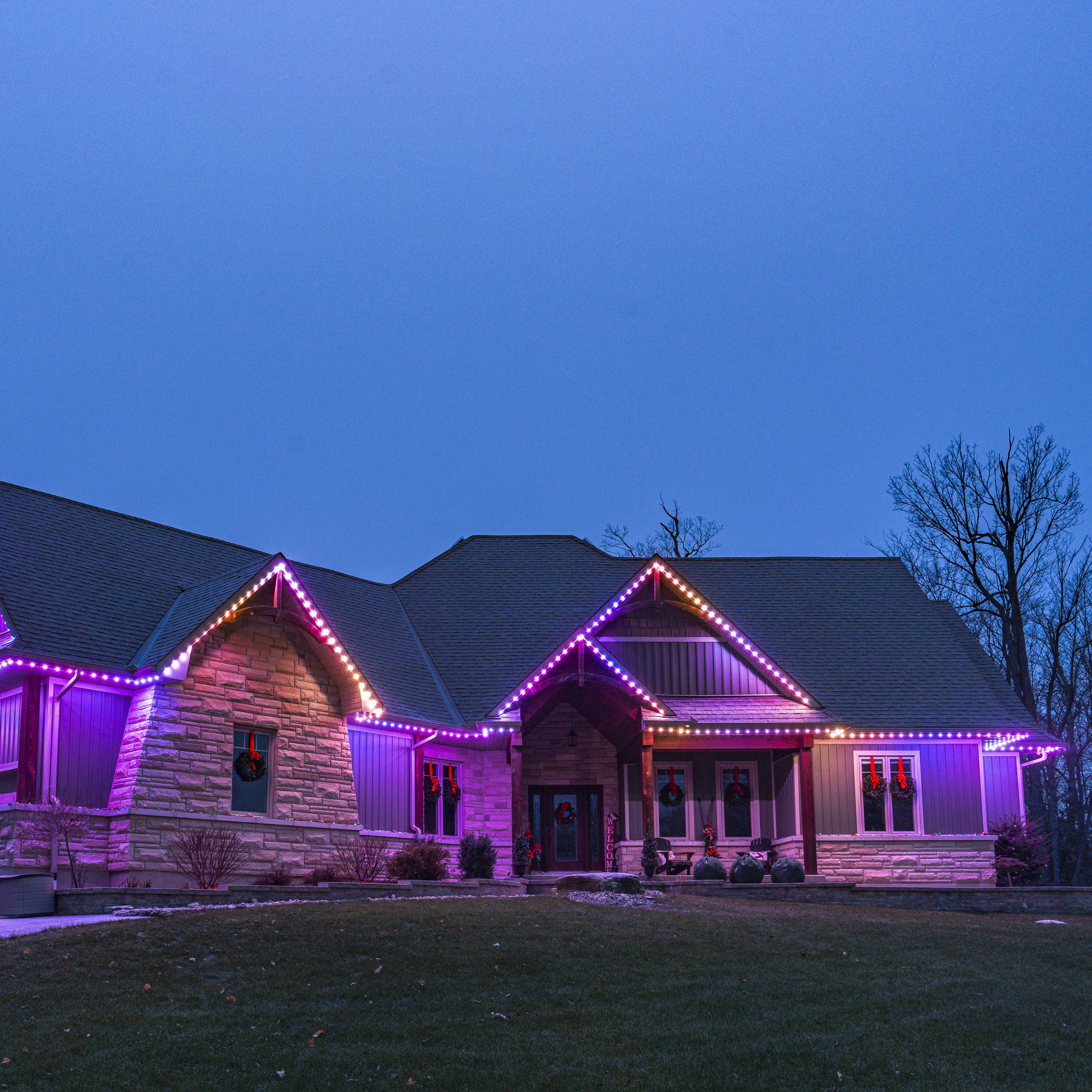 House glowing with festive red permanent Christmas lights at dusk.