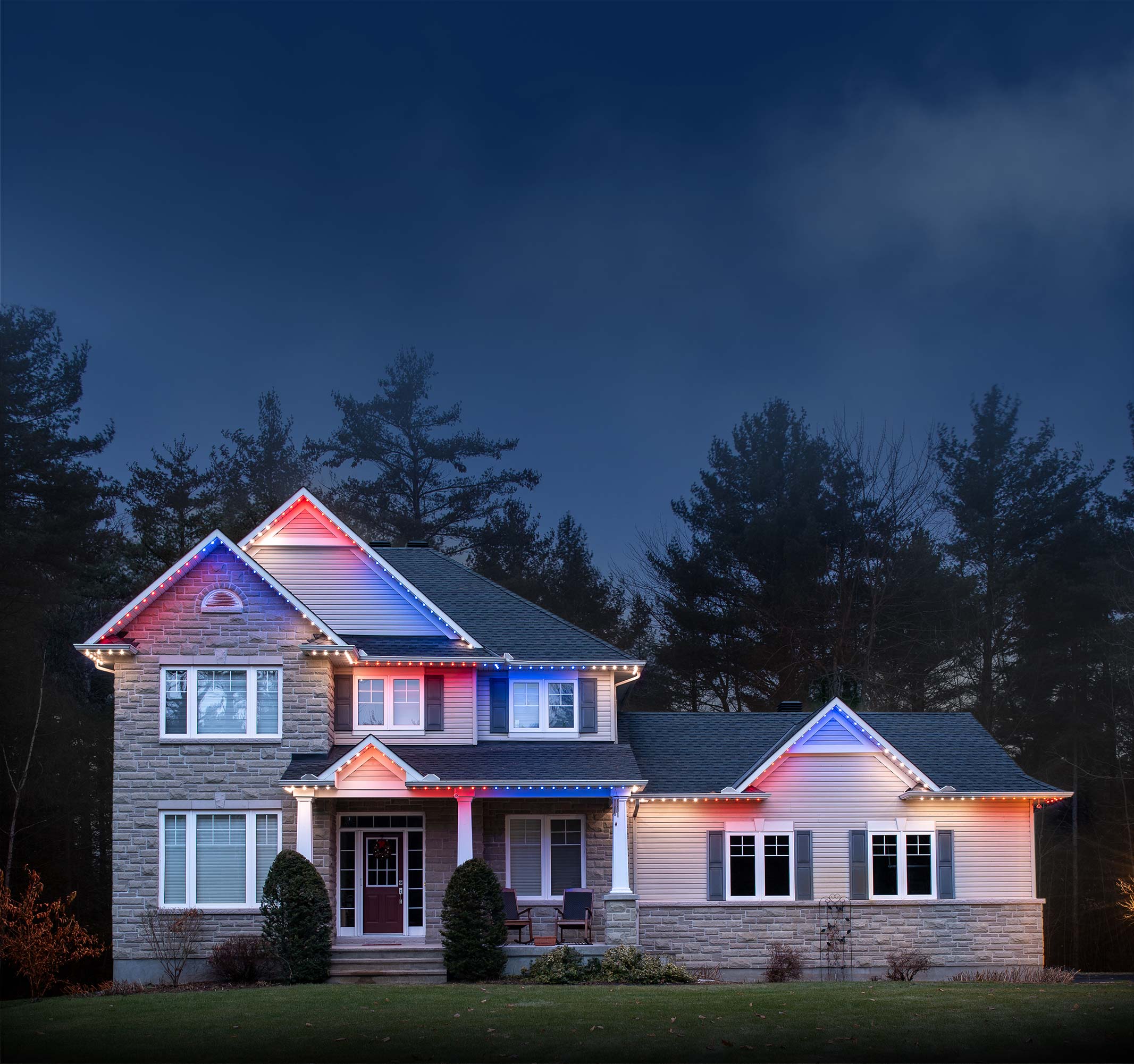 House outlined with red, blue, and white permanent Christmas lights glowing at dusk.