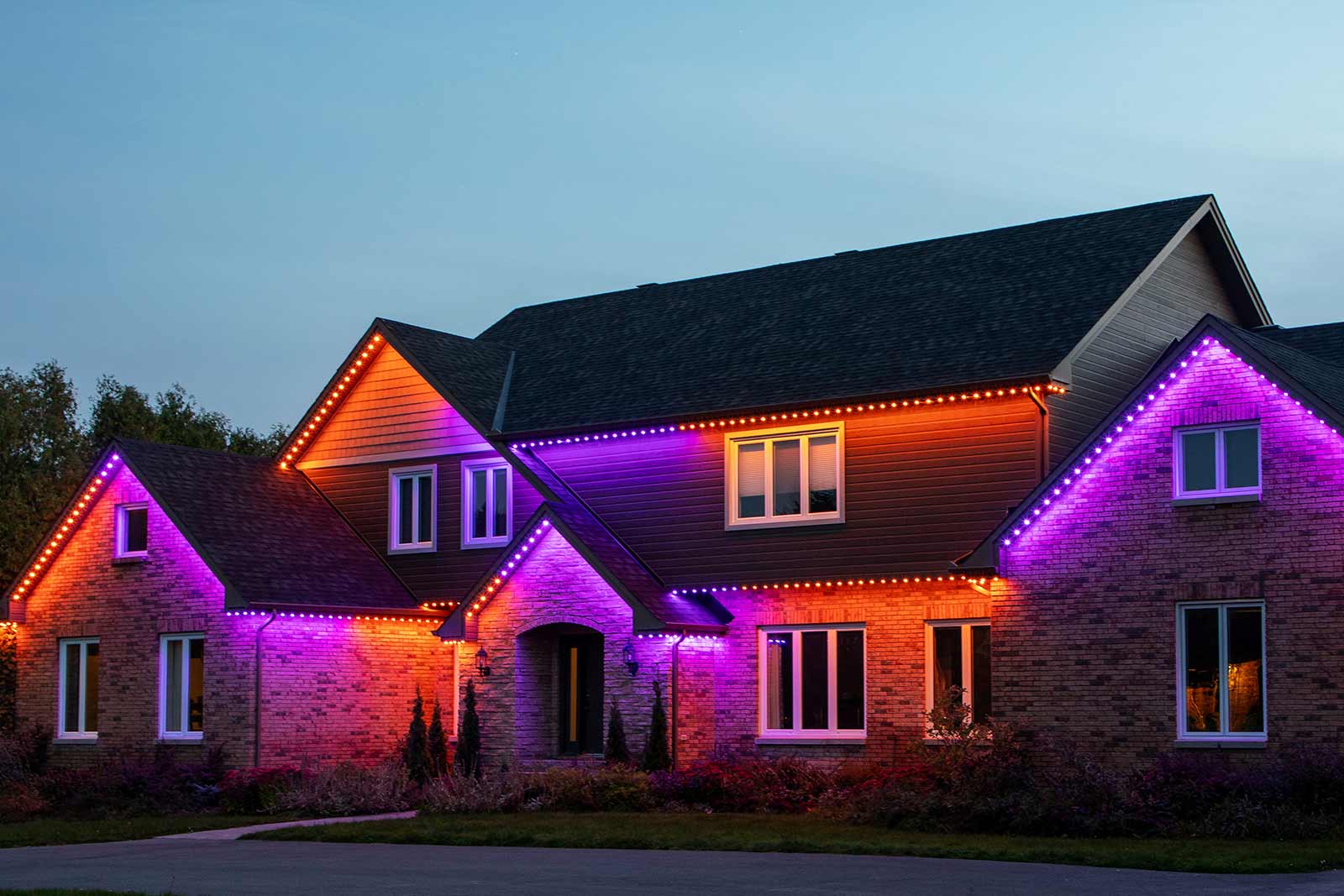 Festive red and white permanent holiday lights illuminating the home at night.