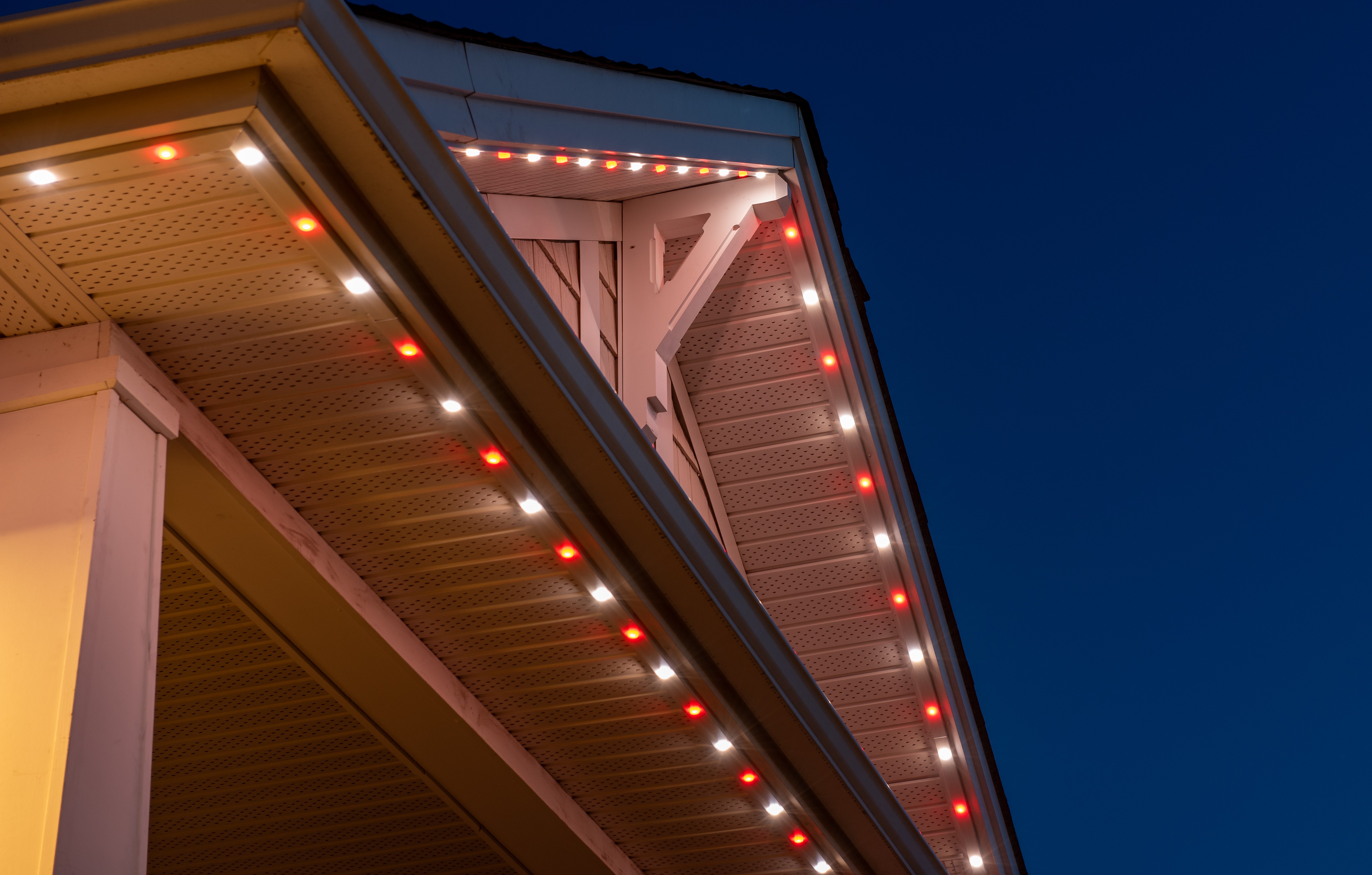 House roofline at dusk with permanent holiday lighting featuring red and white LEDs.