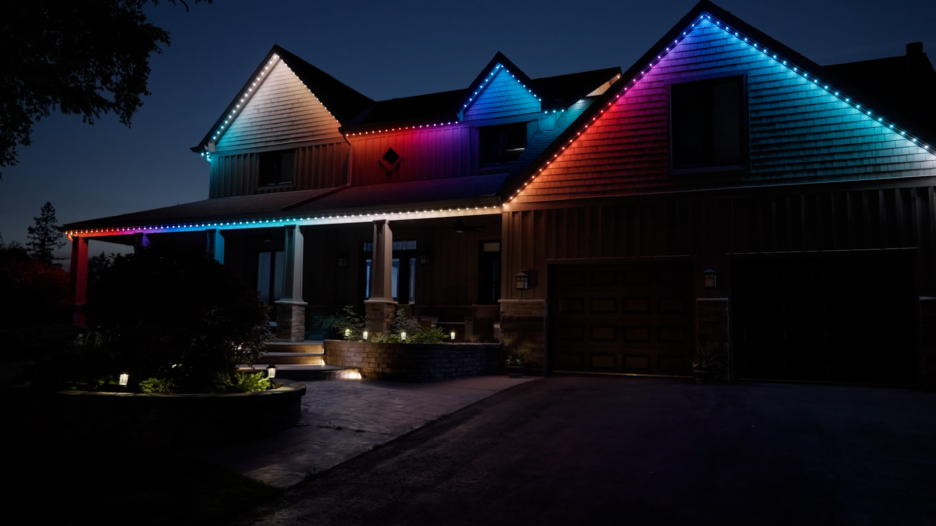 House at dusk illuminated with permanent holiday lighting in multicolor patterns along the roofline.