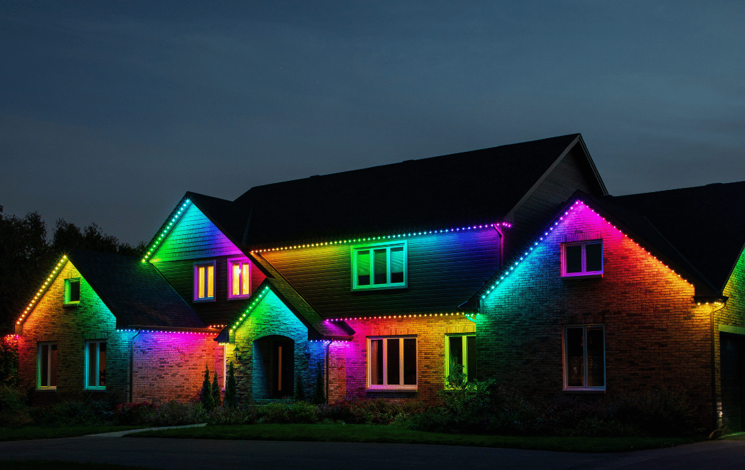 Home exterior illuminated with colorful permanent holiday lights at night.