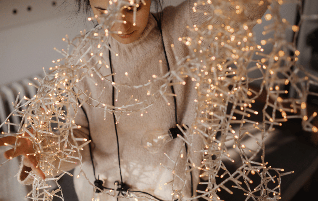 Person untangling warm white holiday string lights indoors.