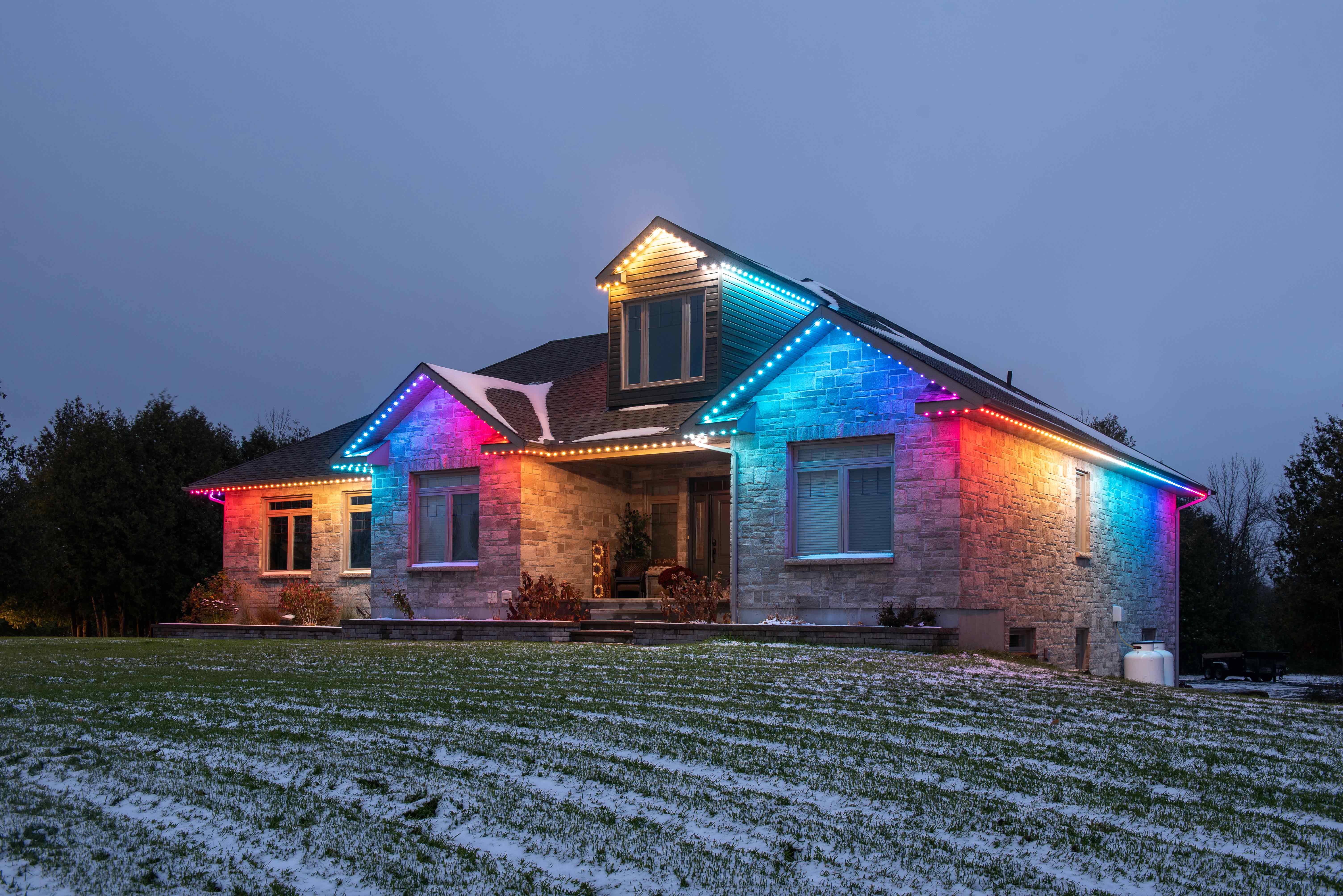 A home at dusk illuminated by colorful permanent outdoor lighting installed along the roofline.