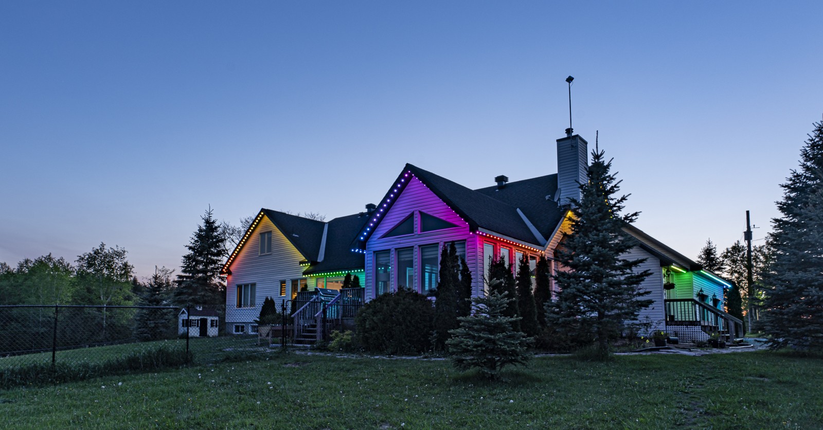 A house at dusk illuminated by colorful permanent outdoor lighting installed along the roofline.