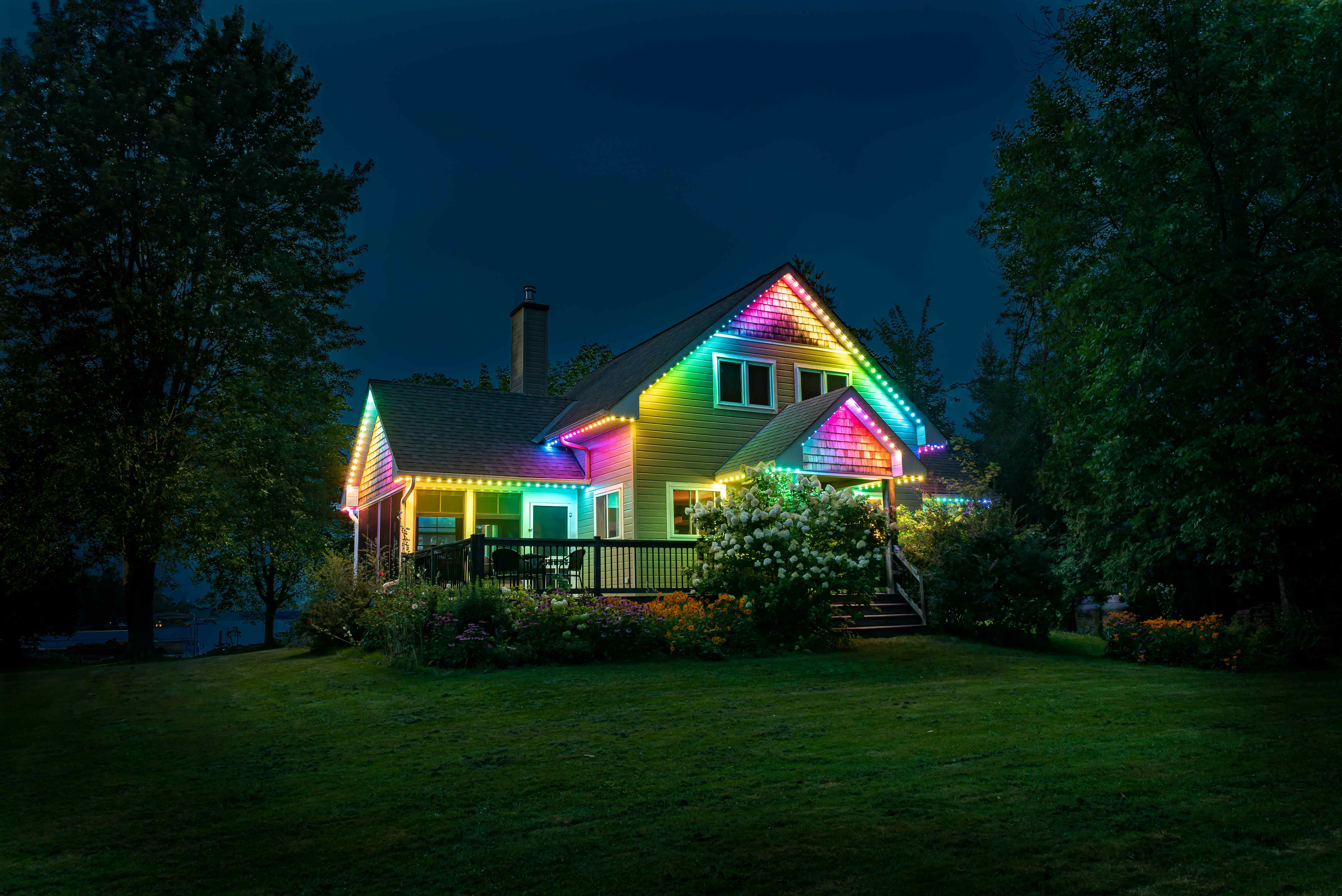 A cottage at night illuminated with colorful permanent outdoor lighting along the roofline.