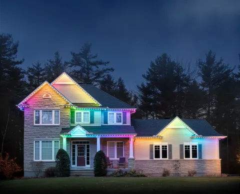 A house with permanent holiday lighting installed, glowing in the rainbow preset