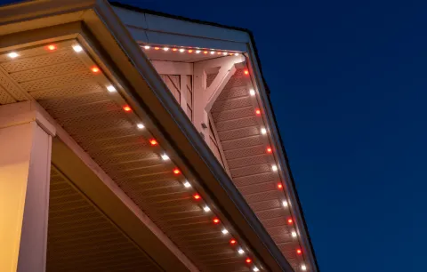 House roofline at dusk with permanent holiday lighting featuring red and white LEDs.