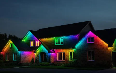 Home exterior illuminated with colorful permanent holiday lights at night.
