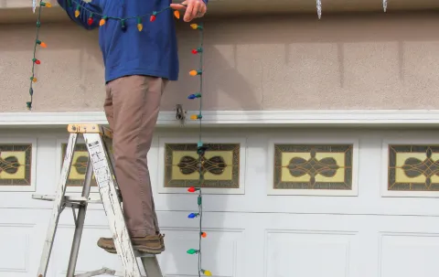 Person standing on a ladder installing temporary Christmas lights