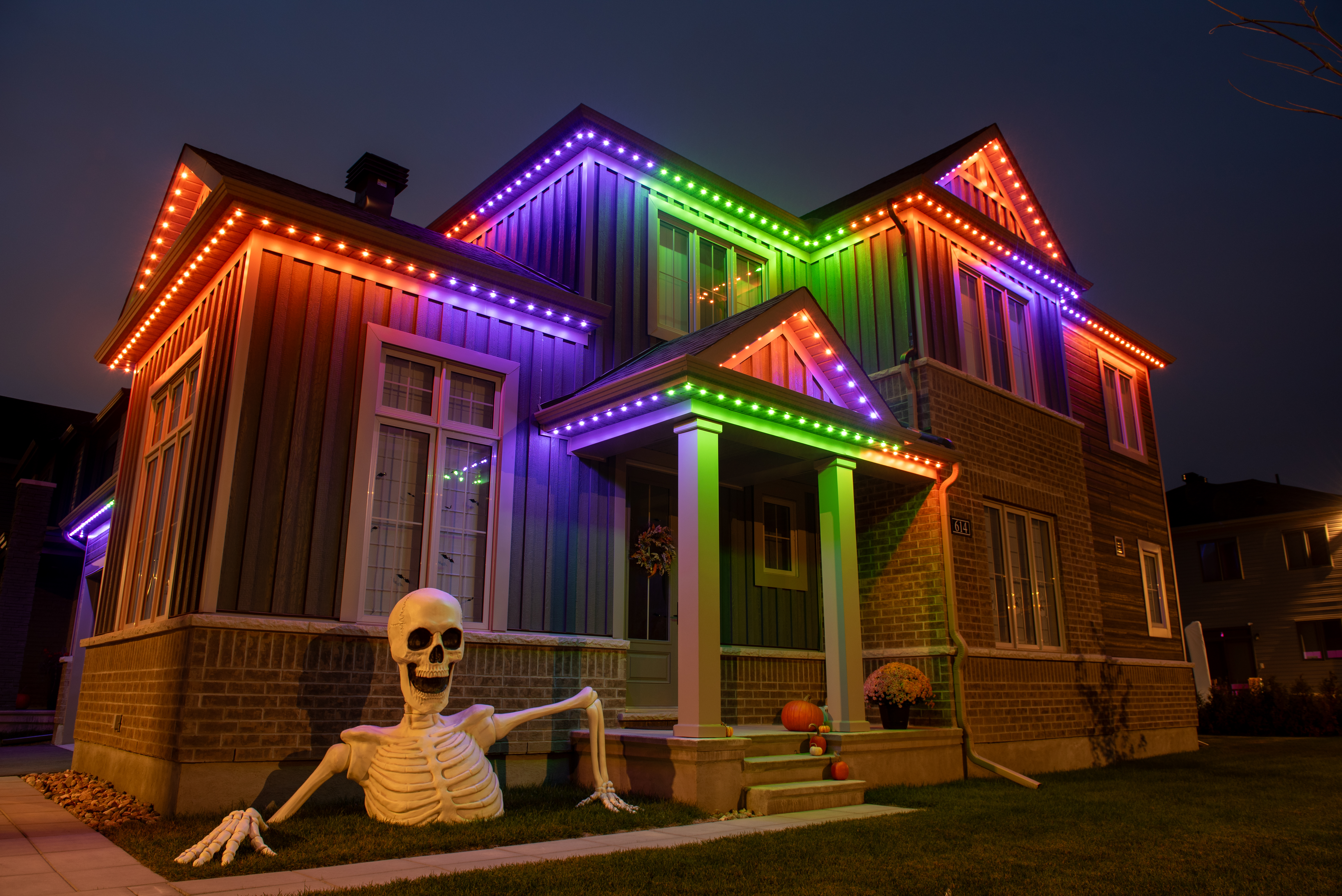 Red, green, and white permanent Christmas lights outlining the roofline of a house in a festive winter scene.